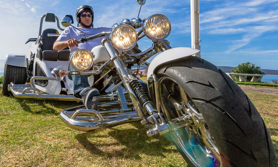 A wide angle, low aspect photo of a man on a white Harley Davidson trike