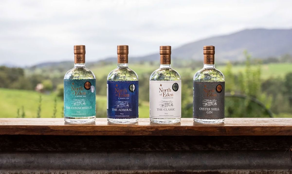 Four bottles of North of Eden gin lined up on an rusty railway girder with rolling green hills in the far distance