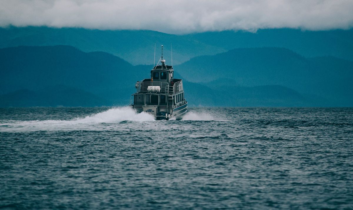 A view of a whale watching boat receding into the distance with dark ominous looking mountains in the far distance