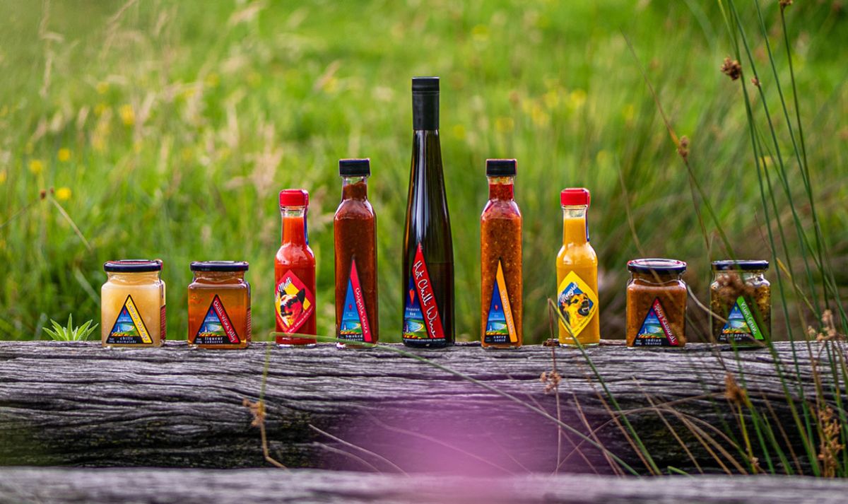 A selection of Disaster Bay Chilli's products lined up along a weathered railway sleeper with native grasses in the background